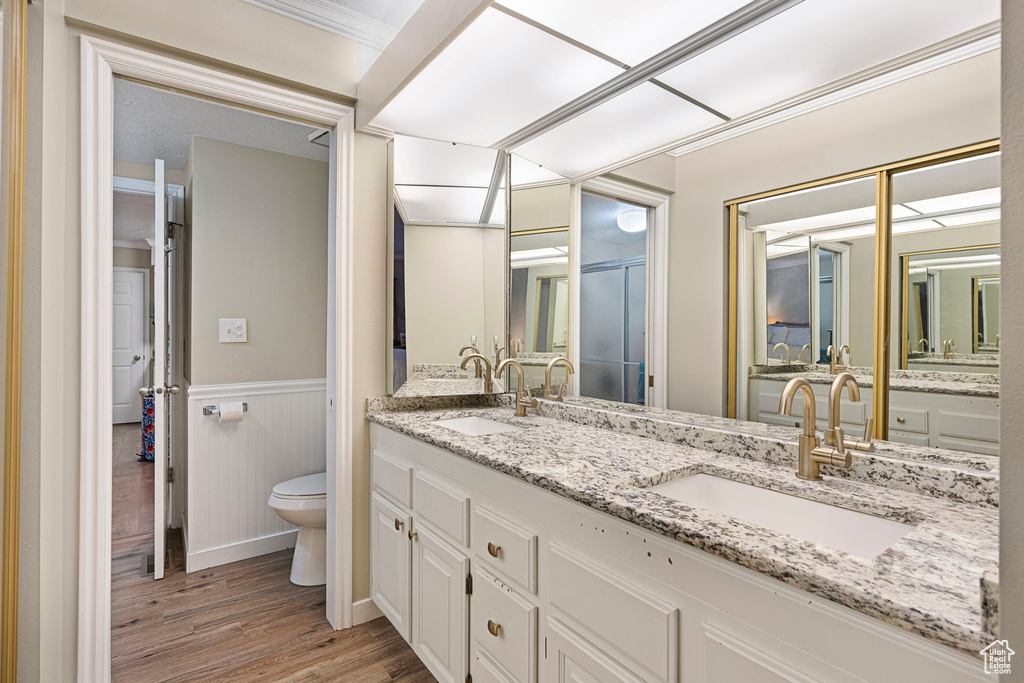 Bathroom with wood-type flooring, ornamental molding, toilet, and double sink vanity