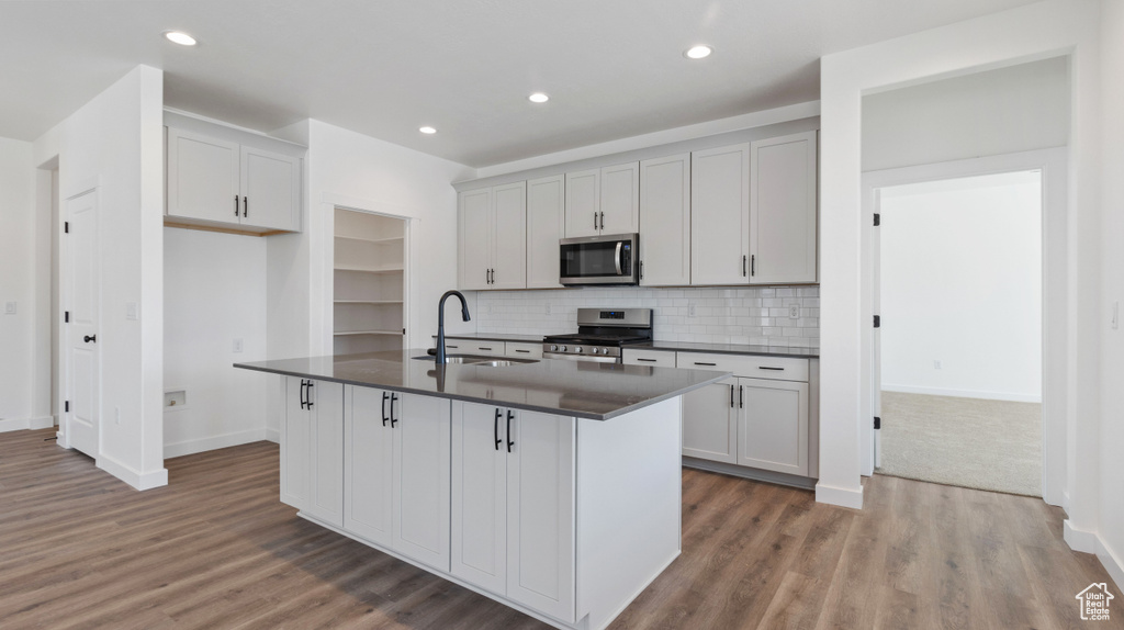 Kitchen featuring hardwood / wood-style flooring, appliances with stainless steel finishes, backsplash, sink, and an island with sink
