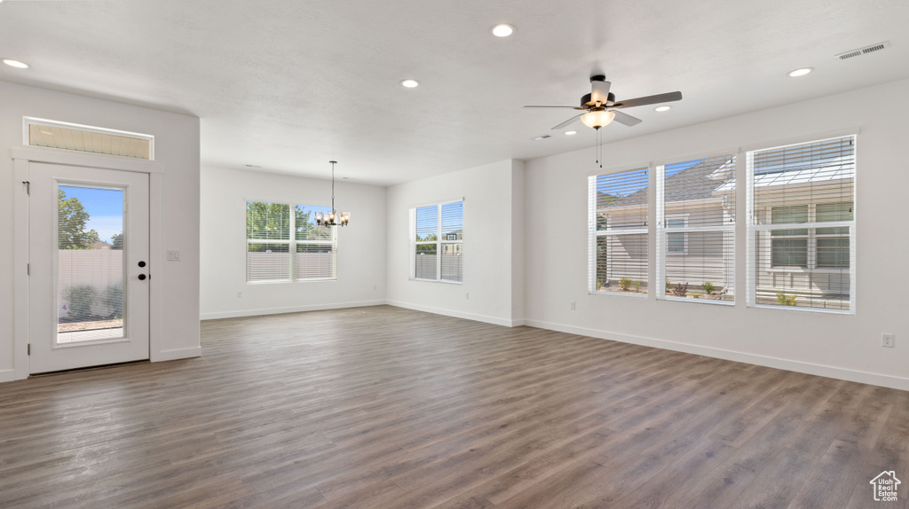 Unfurnished living room with plenty of natural light, ceiling fan with notable chandelier, and dark hardwood / wood-style floors