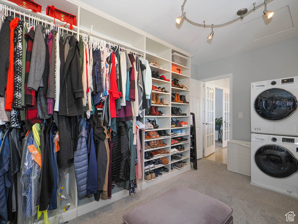 Spacious closet featuring stacked washer / drying machine, light carpet, and french doors