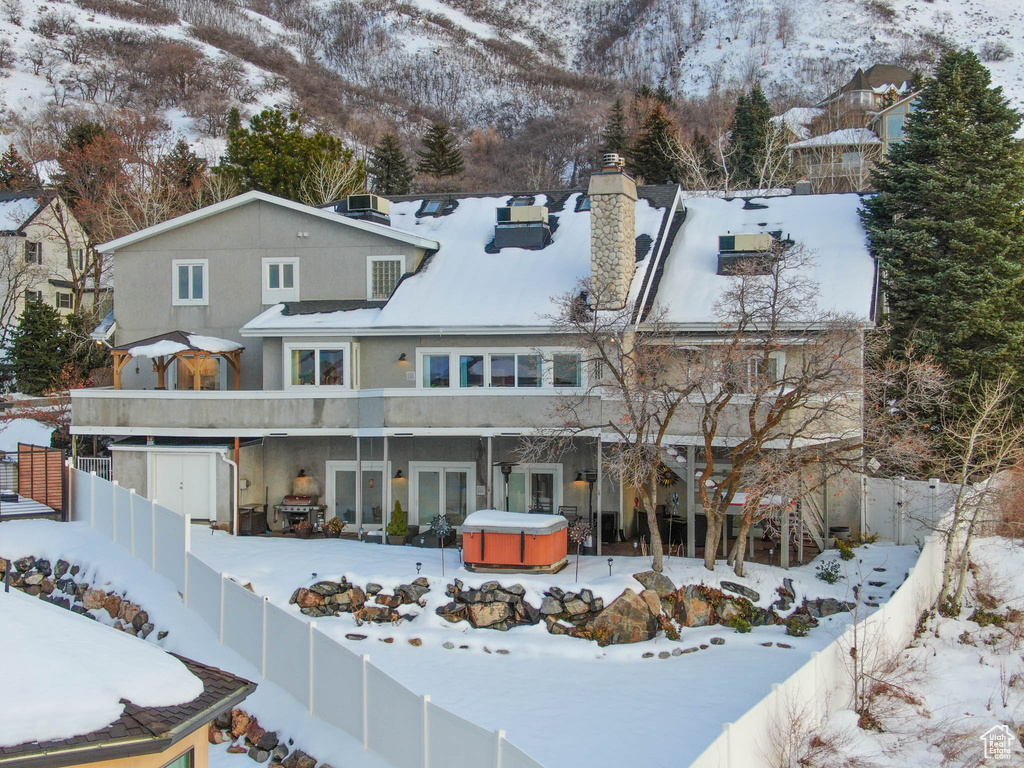 Snow covered rear of property with a mountain view and a hot tub