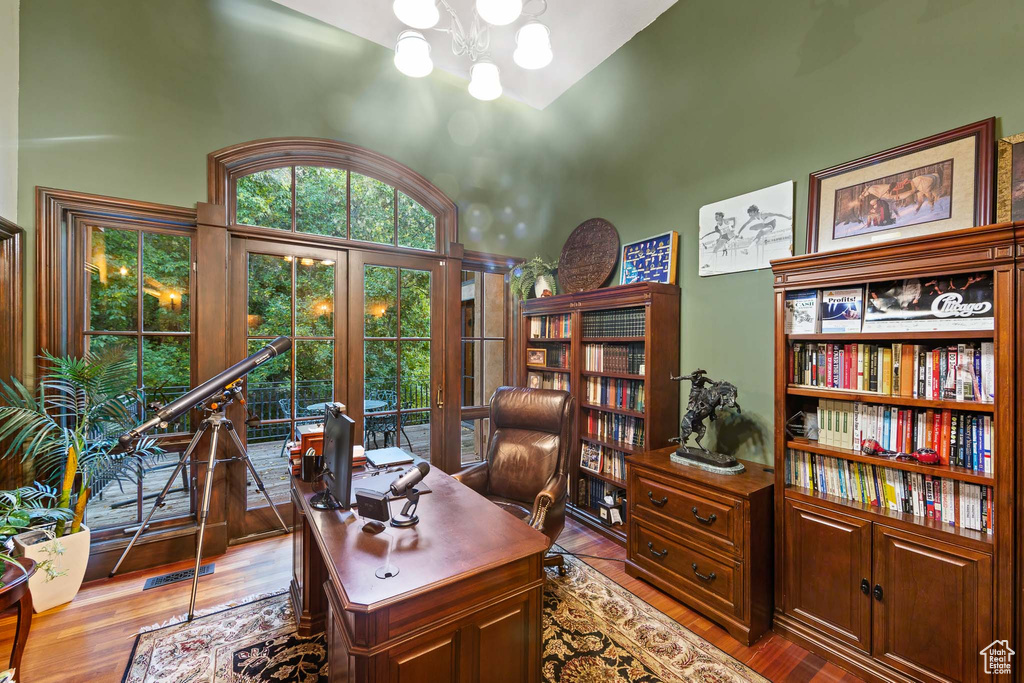 Office area with dark hardwood / wood-style floors, a notable chandelier, a high ceiling, and french doors