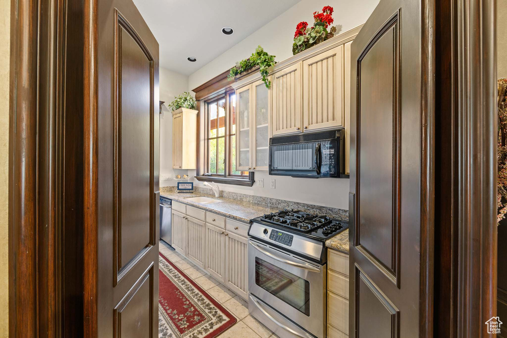 Kitchen with sink, appliances with stainless steel finishes, light stone counters, and light tile floors