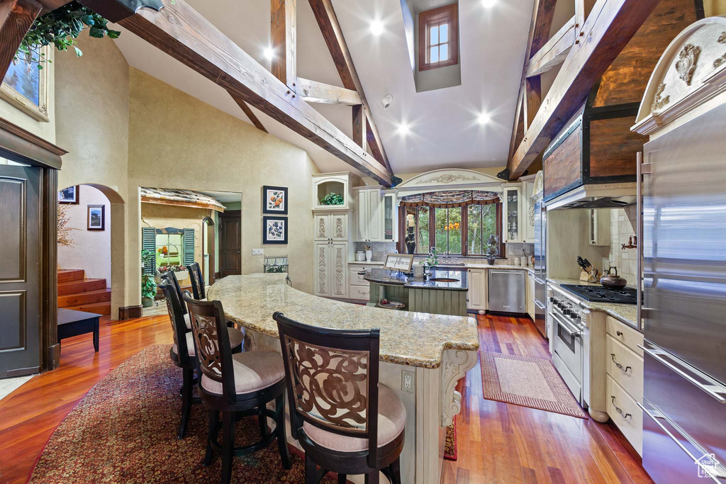 Kitchen with high vaulted ceiling, appliances with stainless steel finishes, a center island, and hardwood / wood-style floors