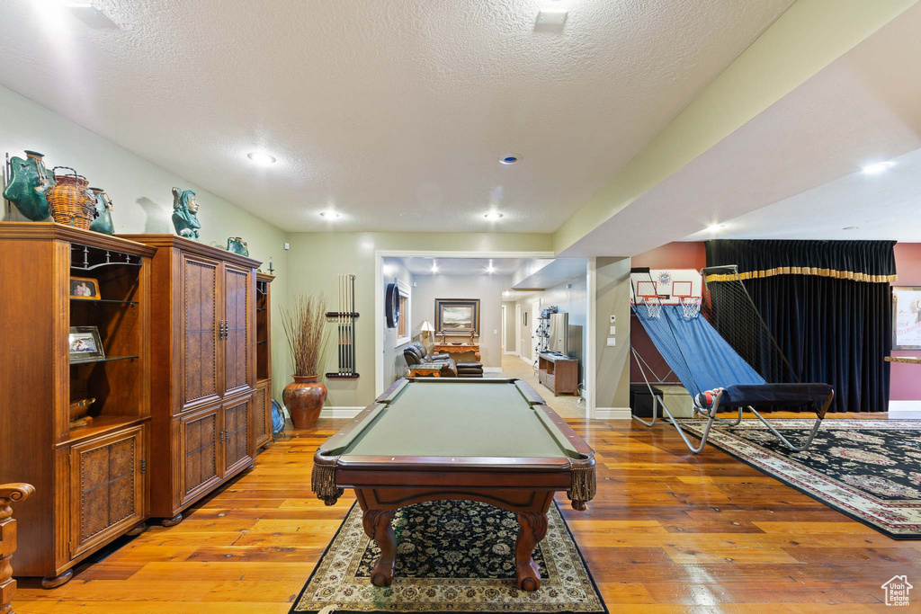 Game room with pool table, a textured ceiling, and light hardwood / wood-style flooring