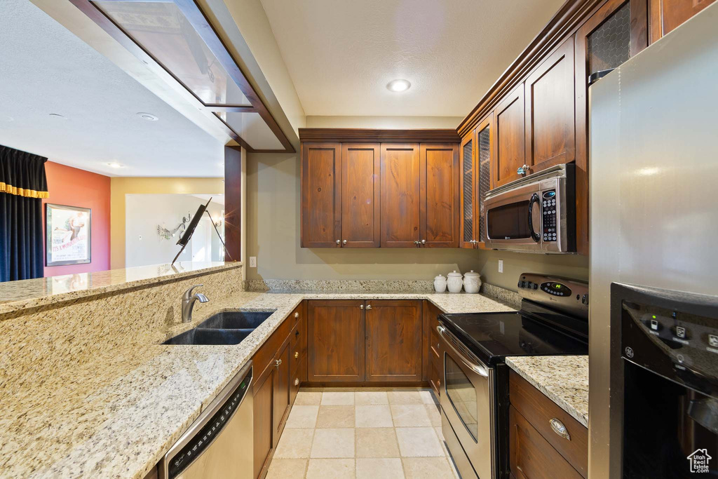 Kitchen featuring sink, stainless steel appliances, light tile flooring, and light stone counters