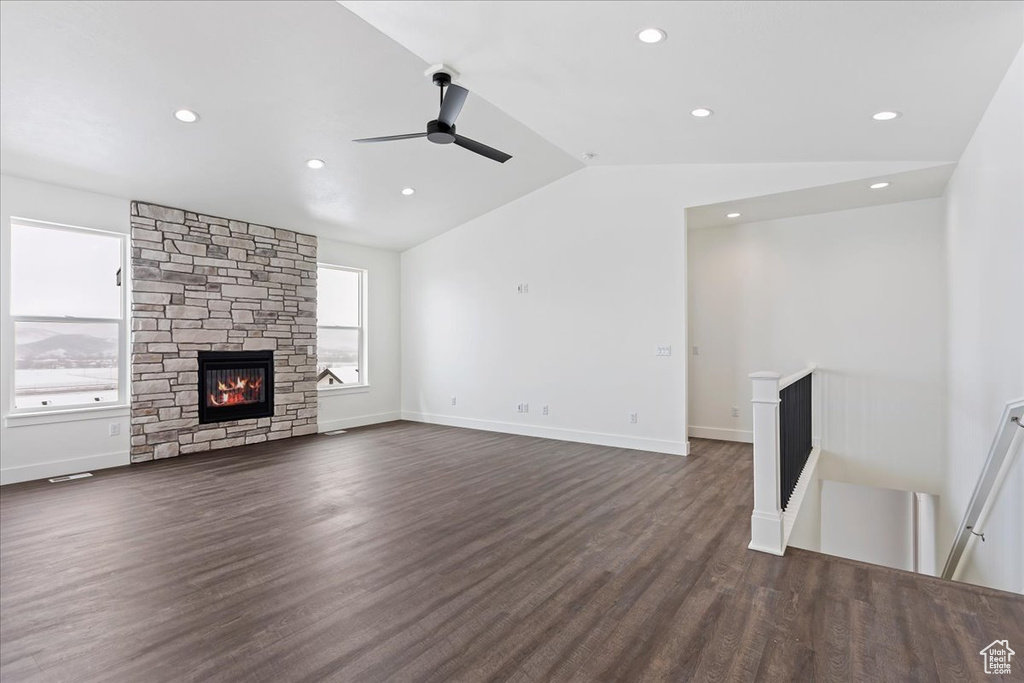 Unfurnished living room featuring dark hardwood / wood-style floors, ceiling fan, vaulted ceiling, and a fireplace