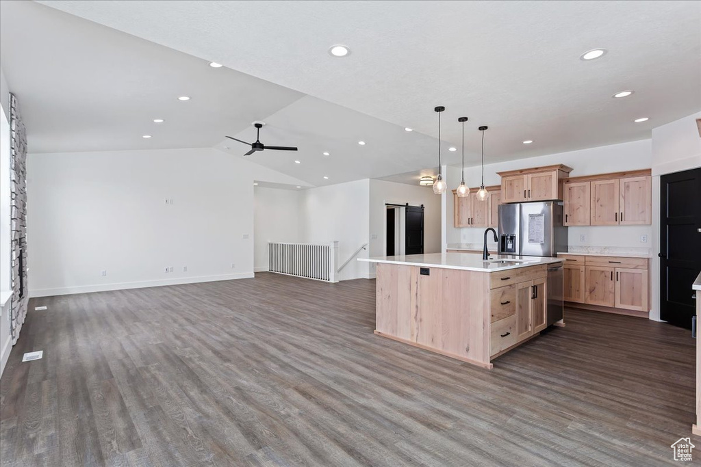 Kitchen with decorative light fixtures, dark wood-type flooring, ceiling fan, stainless steel appliances, and an island with sink