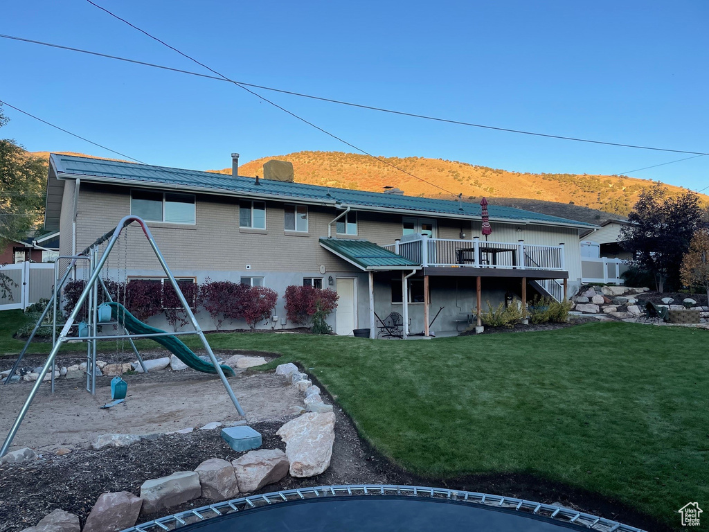 Rear view of house with a deck with mountain view, a playground, and a lawn