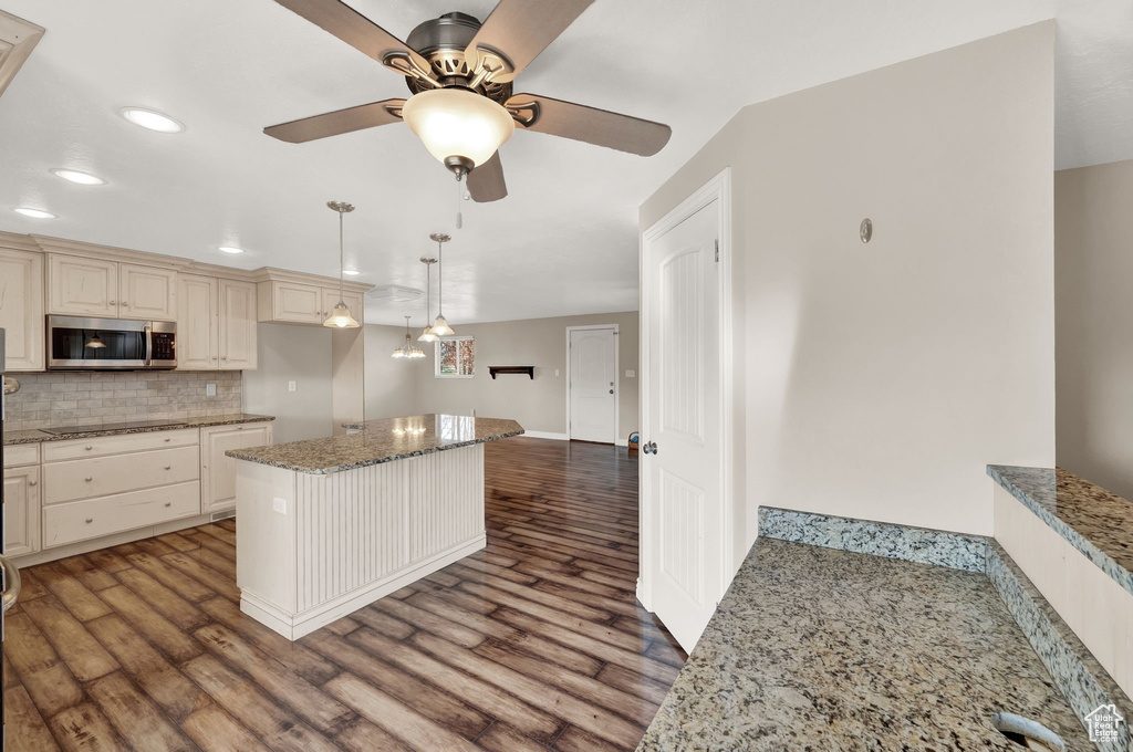 Kitchen featuring light stone counters, ceiling fan, tasteful backsplash, and dark hardwood / wood-style floors
