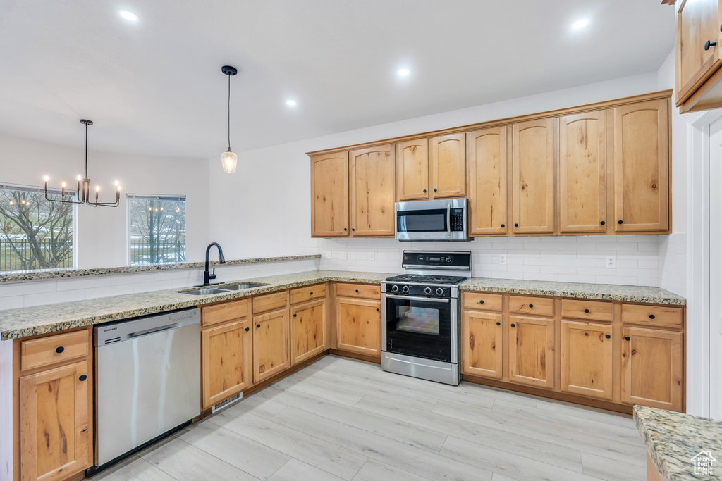 Kitchen featuring pendant lighting, tasteful backsplash, a notable chandelier, appliances with stainless steel finishes, and sink
