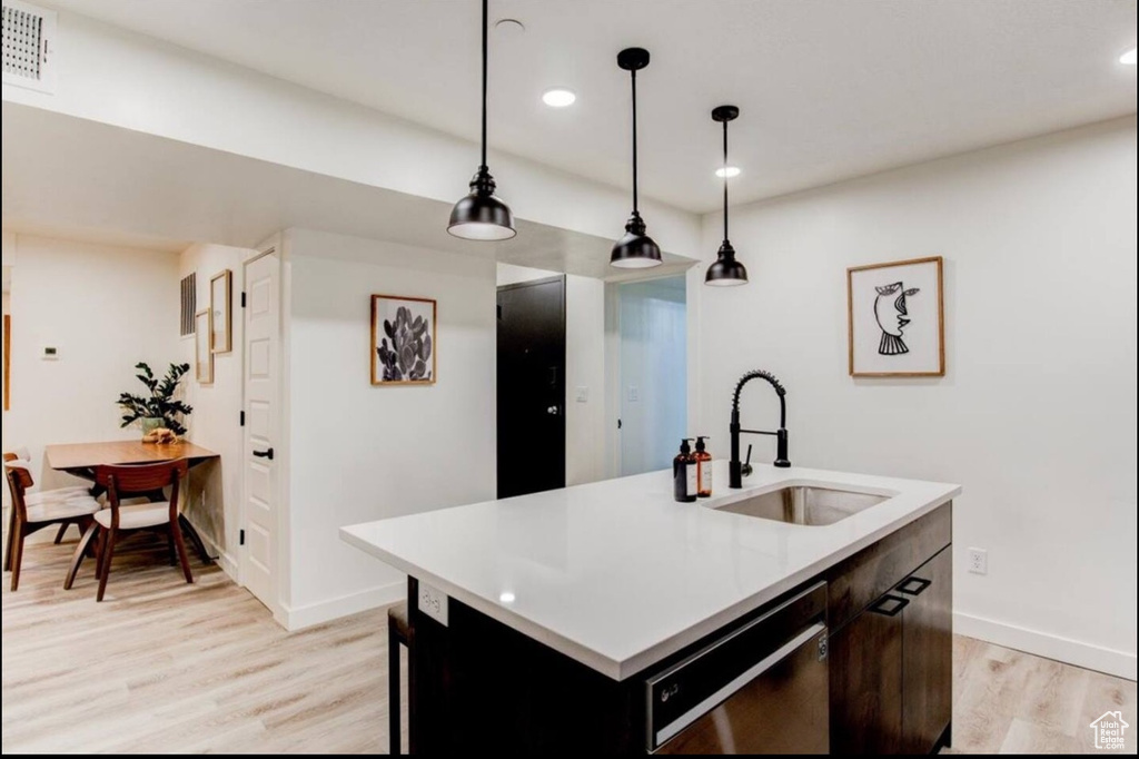 Kitchen featuring light hardwood / wood-style floors, a center island with sink, decorative light fixtures, dishwasher, and sink