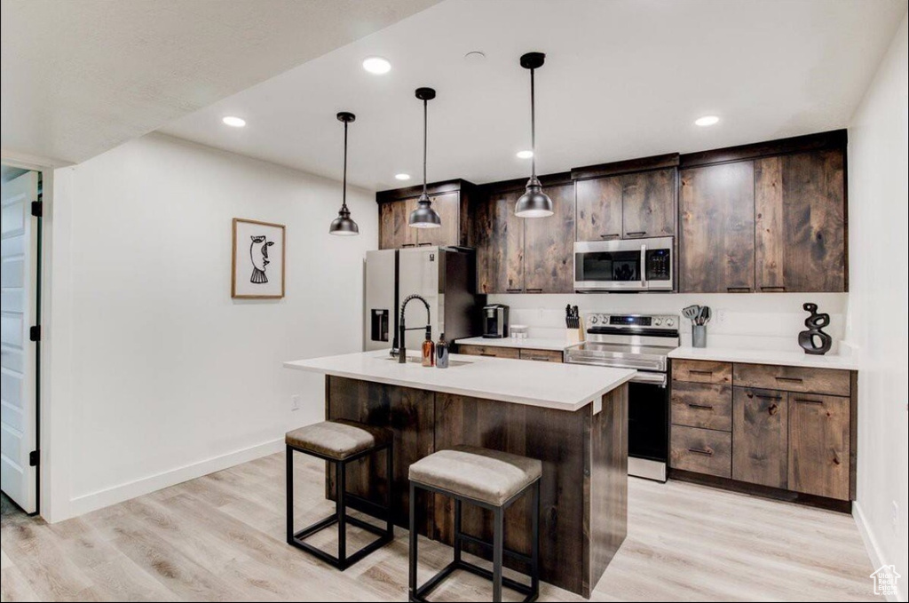 Kitchen with refrigerator with ice dispenser, dark brown cabinetry, light hardwood / wood-style flooring, electric range oven, and an island with sink