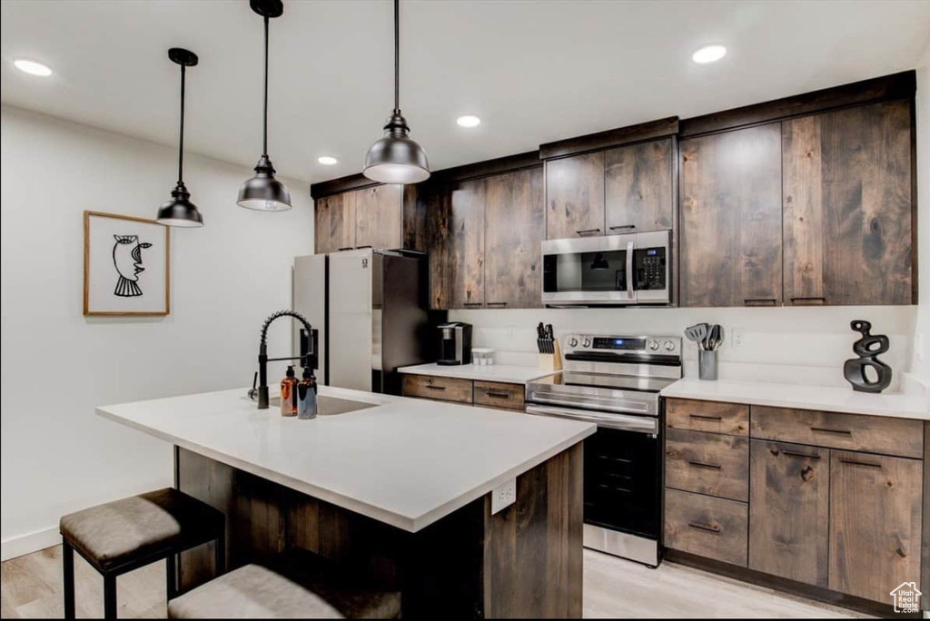 Kitchen featuring appliances with stainless steel finishes, pendant lighting, an island with sink, sink, and light wood-type flooring