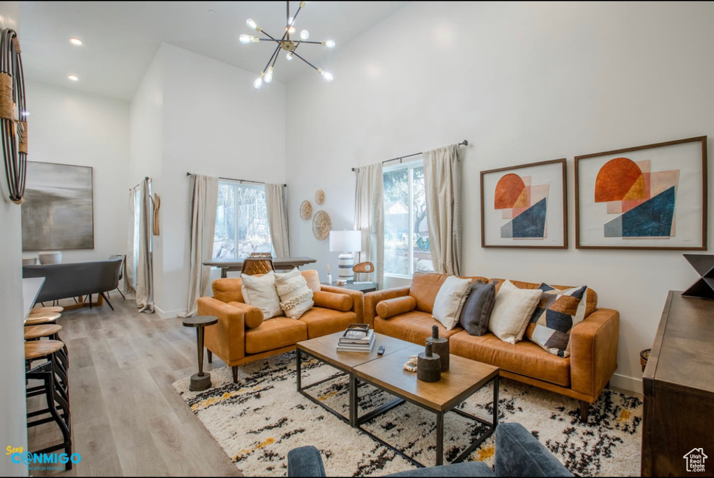 Living room featuring high vaulted ceiling, a wealth of natural light, a notable chandelier, and light hardwood / wood-style flooring