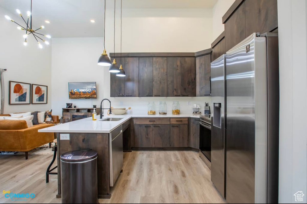 Kitchen featuring appliances with stainless steel finishes, pendant lighting, light hardwood / wood-style flooring, a notable chandelier, and sink