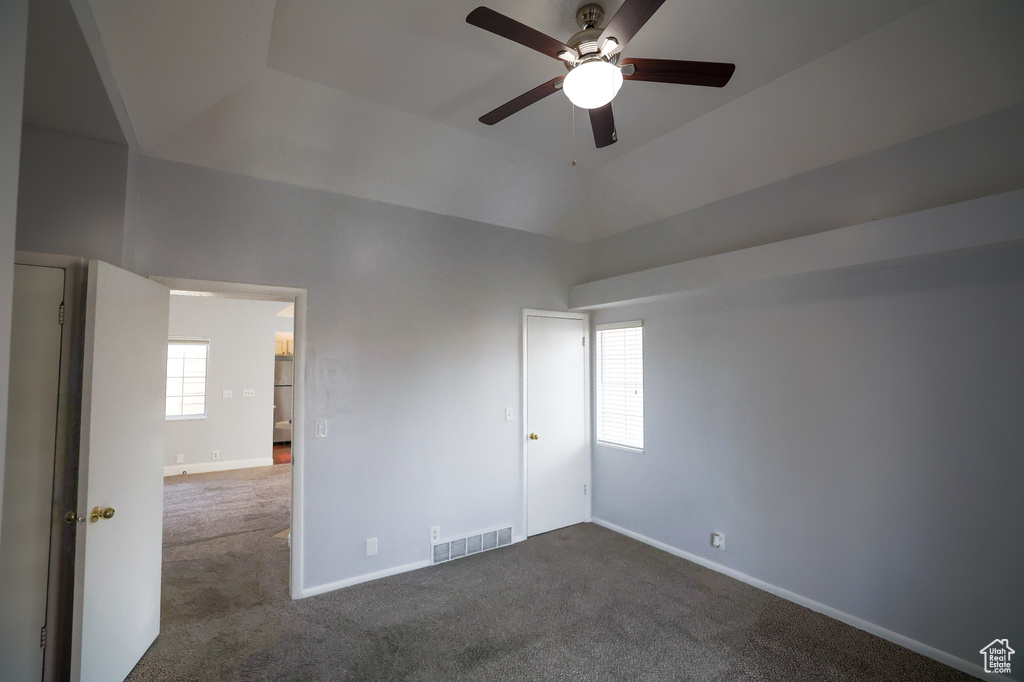 Unfurnished bedroom featuring a tray ceiling, dark colored carpet, and ceiling fan