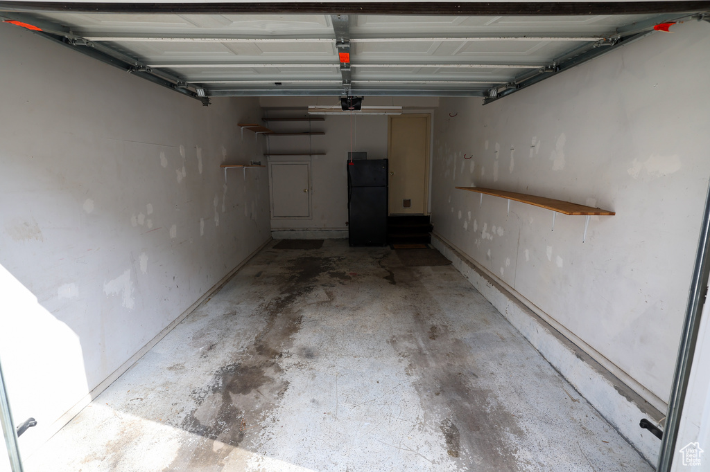 Garage with a garage door opener and black refrigerator