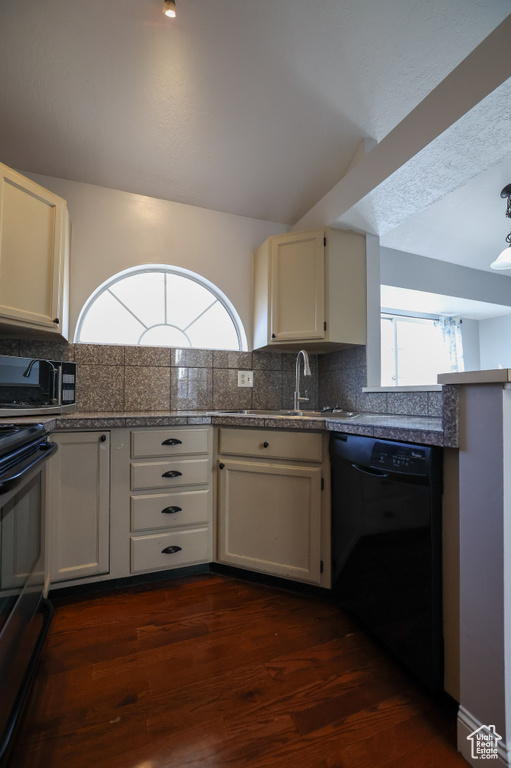 Kitchen with tasteful backsplash, cream cabinets, black appliances, and dark hardwood / wood-style flooring