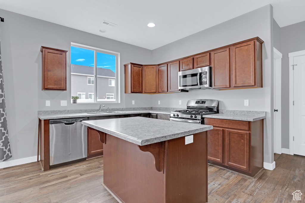 Kitchen with a breakfast bar, light hardwood / wood-style floors, a center island, stainless steel appliances, and sink