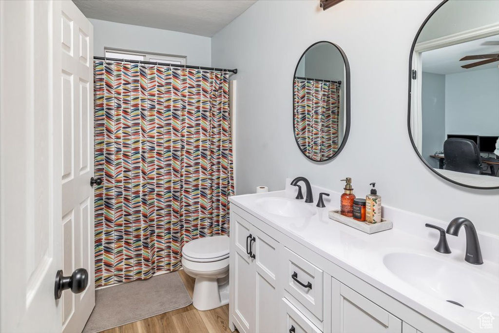 Bathroom featuring toilet, dual vanity, hardwood / wood-style flooring, and ceiling fan