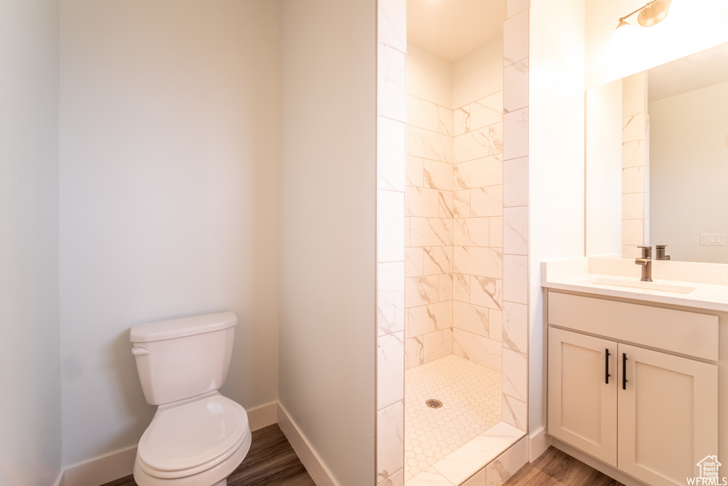 Bathroom featuring vanity, toilet, a tile shower, and hardwood / wood-style flooring