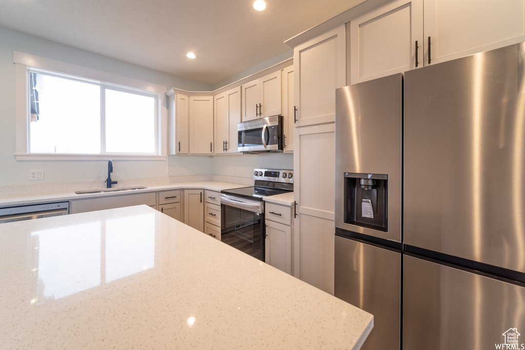 Kitchen featuring white cabinets, sink, light stone countertops, and stainless steel appliances