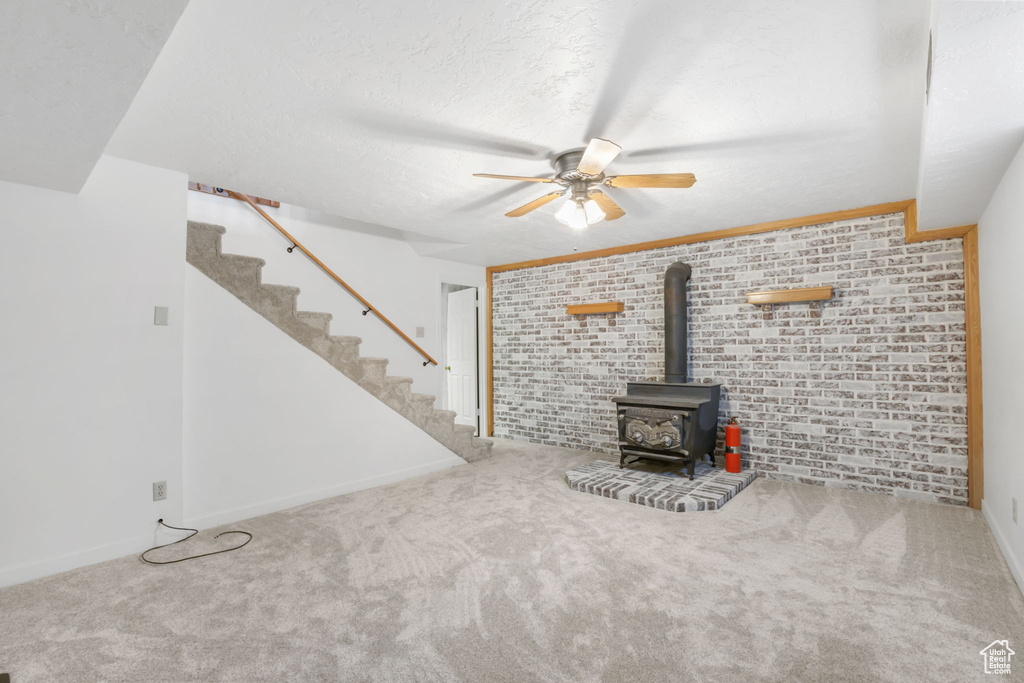 Unfurnished living room with a wood stove, carpet floors, brick wall, and ceiling fan