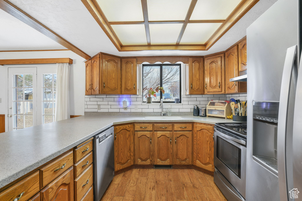 Kitchen featuring appliances with stainless steel finishes, light hardwood / wood-style flooring, backsplash, sink, and a raised ceiling