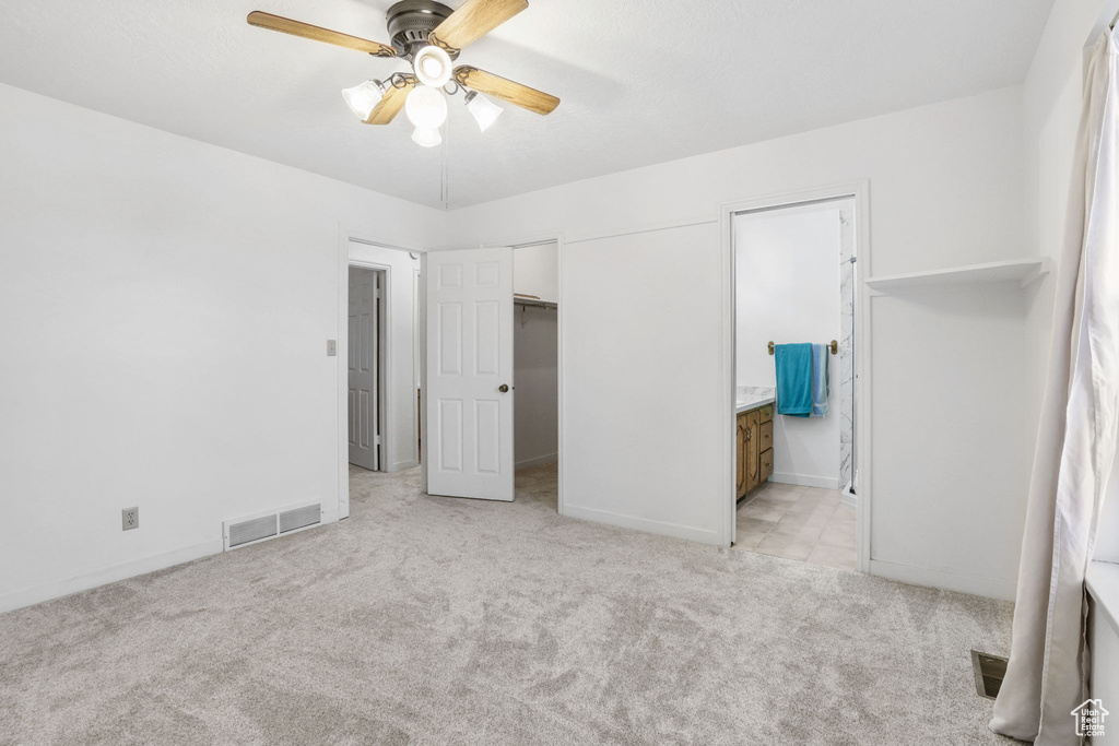 Unfurnished bedroom with light colored carpet, a closet, ensuite bathroom, and ceiling fan