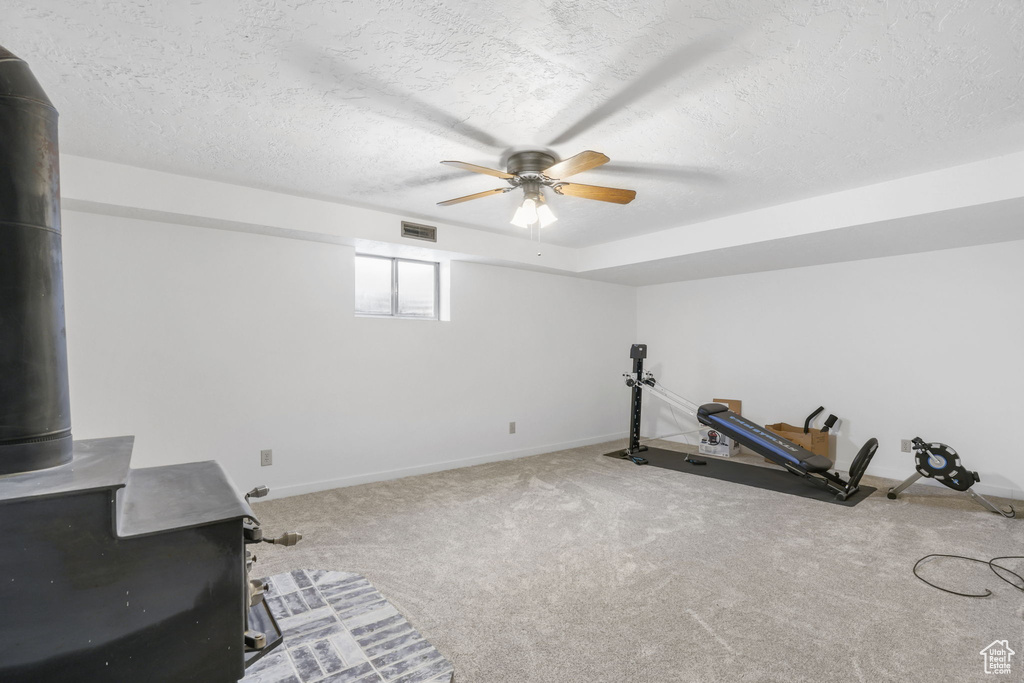 Exercise area with light carpet, a wood stove, a textured ceiling, and ceiling fan