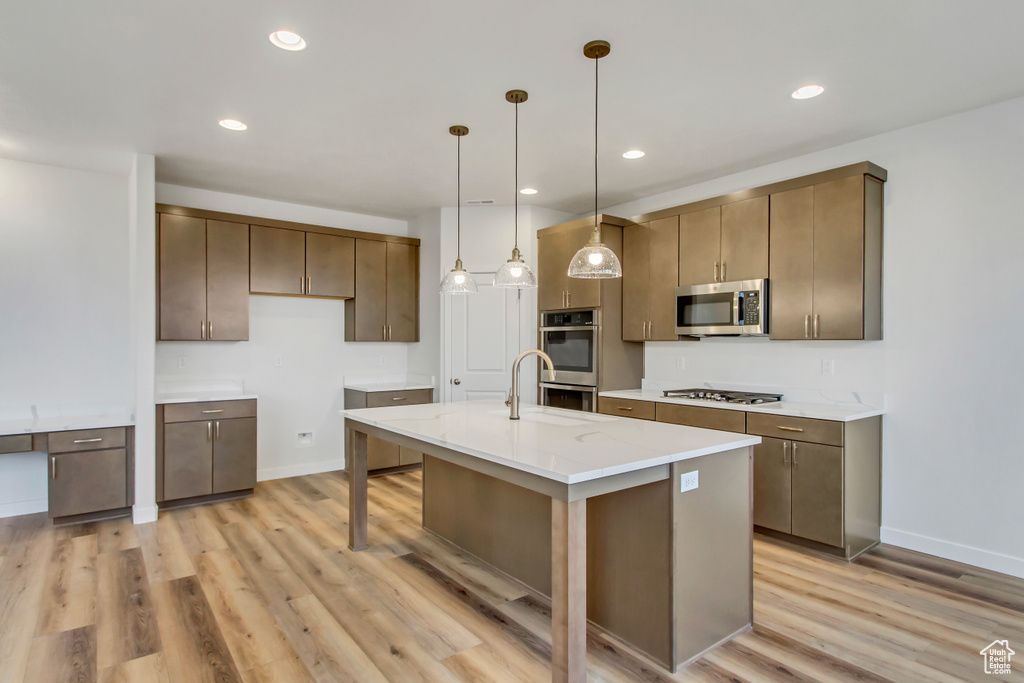 Kitchen with hanging light fixtures, a kitchen breakfast bar, light hardwood / wood-style flooring, stainless steel appliances, and a center island with sink