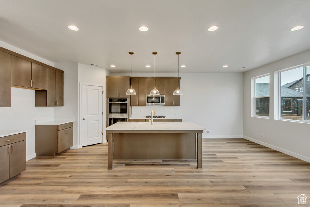 Kitchen featuring stainless steel appliances, decorative light fixtures, a breakfast bar, light hardwood / wood-style flooring, and a kitchen island with sink