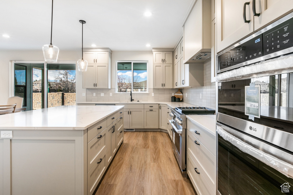 Kitchen featuring a kitchen island, custom exhaust hood, tasteful backsplash, light hardwood / wood-style floors, and appliances with stainless steel finishes