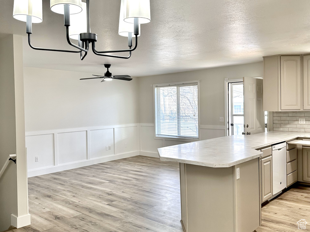 Kitchen featuring kitchen peninsula, ceiling fan with notable chandelier, light hardwood / wood-style floors, white dishwasher, and tasteful backsplash