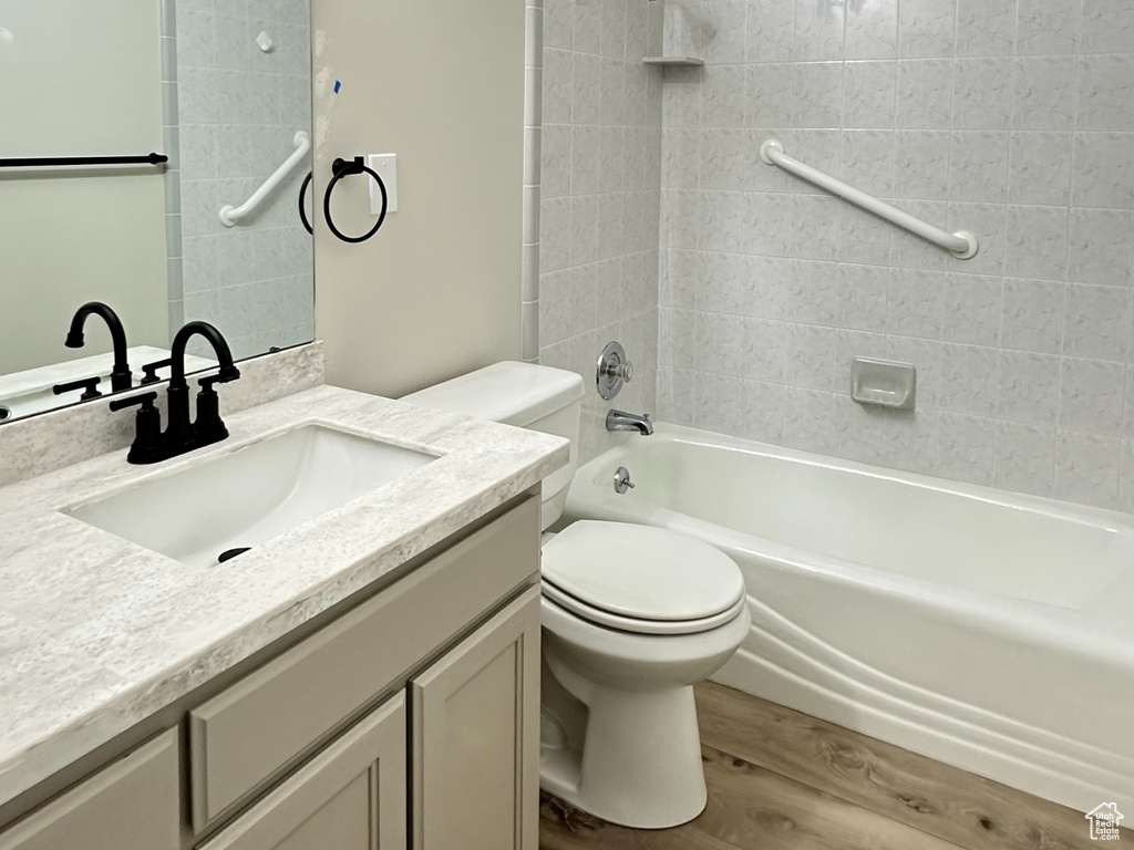 Full bathroom with wood-type flooring, tiled shower / bath, toilet, and vanity