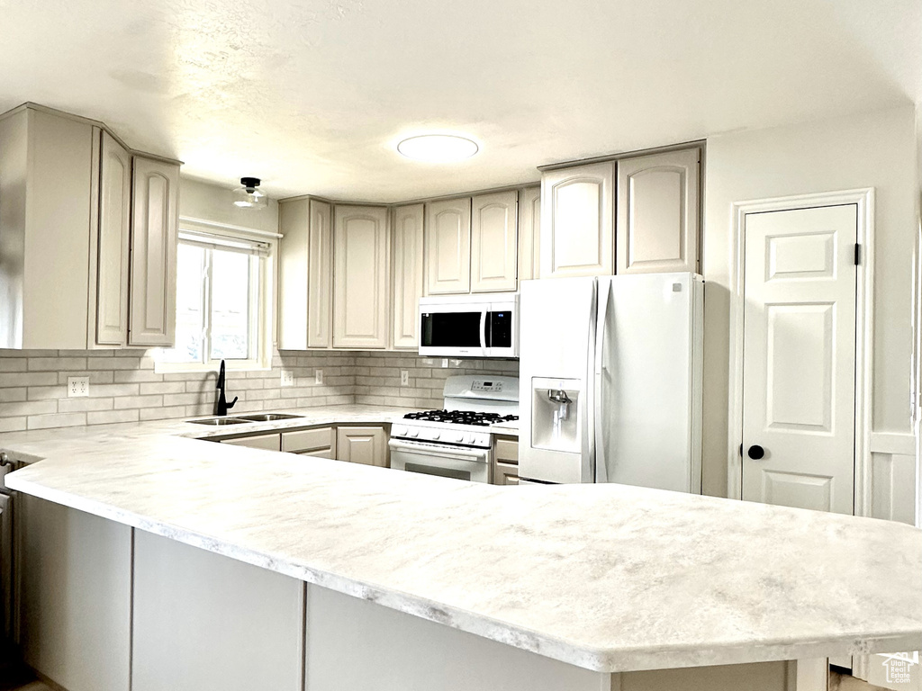 Kitchen featuring kitchen peninsula, white appliances, light stone counters, sink, and tasteful backsplash