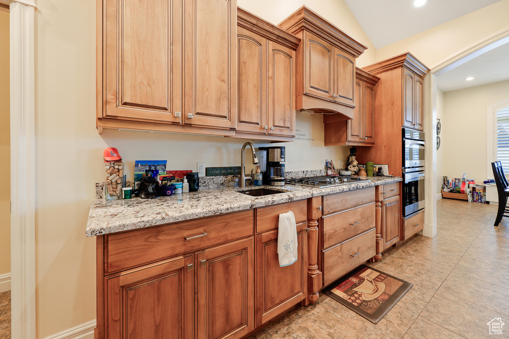 Kitchen featuring light tile floors, light stone countertops, vaulted ceiling, sink, and stainless steel appliances