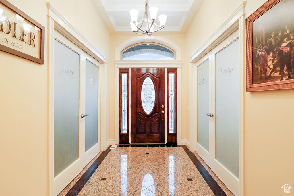 Entryway featuring crown molding, a tray ceiling, an inviting chandelier, and dark tile floors