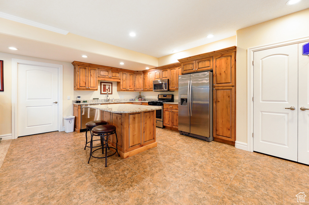 Kitchen featuring a kitchen breakfast bar, light tile floors, light stone counters, appliances with stainless steel finishes, and a center island