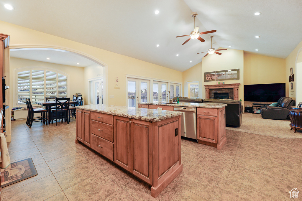 Kitchen with ceiling fan, stainless steel dishwasher, light stone countertops, light tile flooring, and a center island