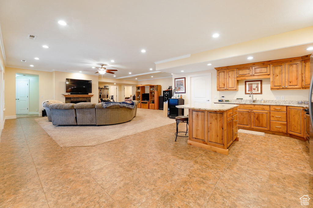 Kitchen featuring a kitchen island, light tile floors, ceiling fan, a breakfast bar area, and light stone counters