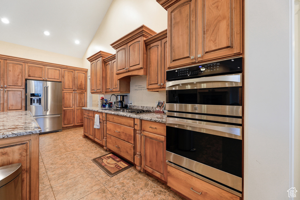 Kitchen featuring stainless steel appliances, vaulted ceiling, light stone counters, and light tile flooring