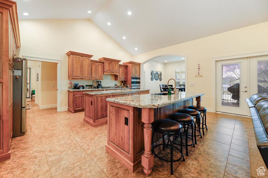 Kitchen featuring light tile flooring, a breakfast bar area, french doors, sink, and a kitchen island with sink