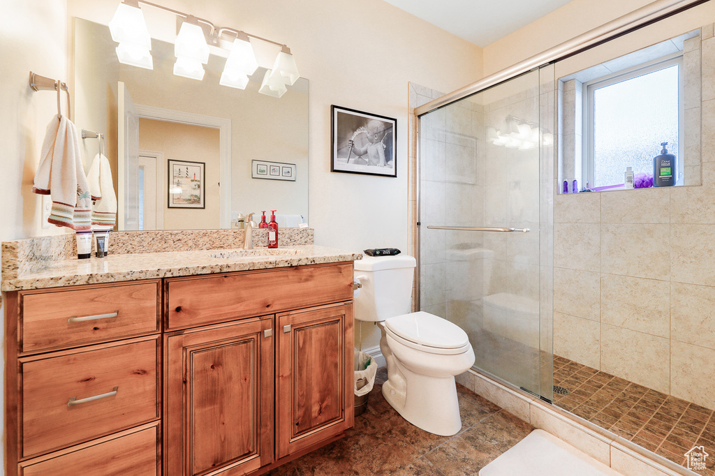 Bathroom with a shower with shower door, oversized vanity, toilet, and tile flooring