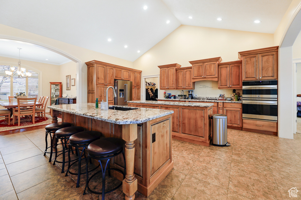 Kitchen with a breakfast bar, light stone countertops, a notable chandelier, a center island with sink, and stainless steel appliances