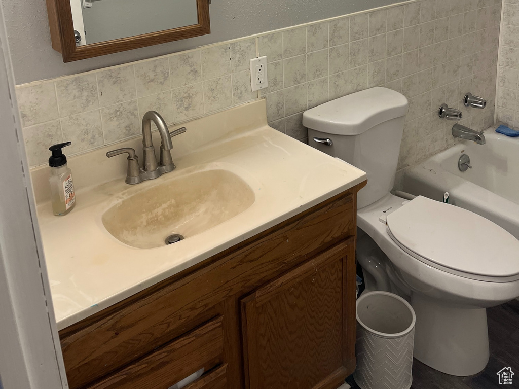 Bathroom featuring tasteful backsplash, toilet, vanity with extensive cabinet space, and tile walls
