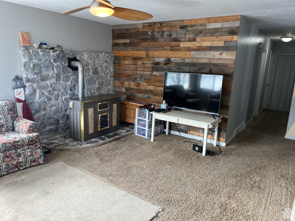 Living room with wood walls, a wood stove, dark carpet, and ceiling fan