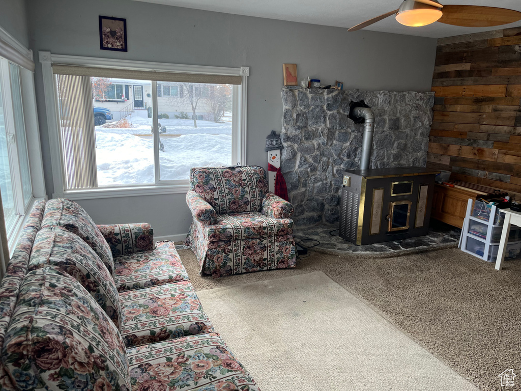 Carpeted living room with wooden walls, a wood stove, and ceiling fan