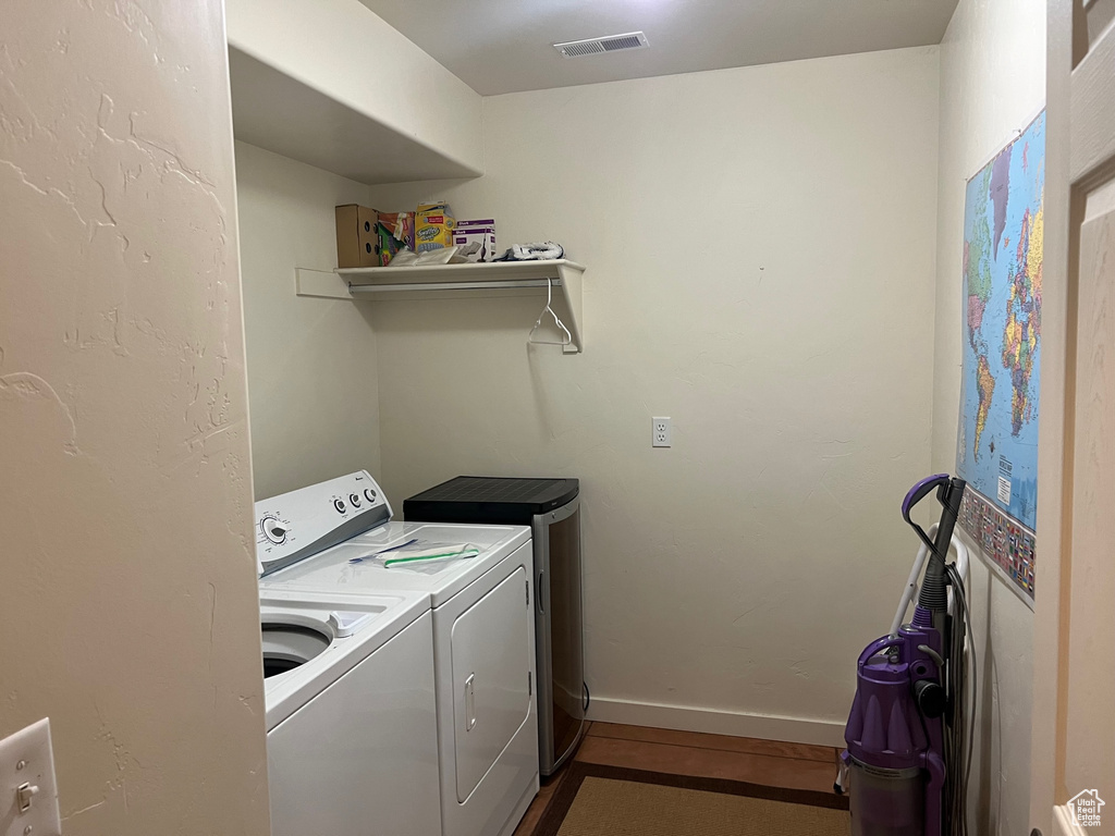 Clothes washing area with washer and clothes dryer and dark wood-type flooring